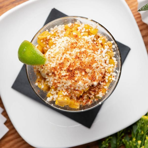Elote in a glass, topped with cotija cheese, chili powder, and a lime wedge.
