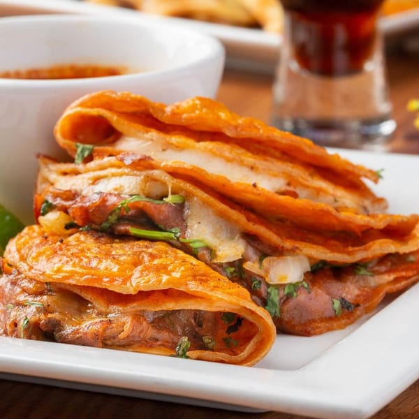 Three golden-brown birria tacos with melted cheese and cilantro, served with a side of consommé.