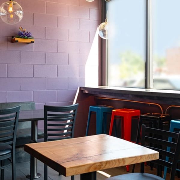 Interior of Mezcal Mexican Bar & Kitchen with wooden tables, black chairs, and colorful bar stools.