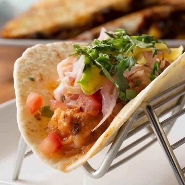 A close-up of a Mezcal Mexican shrimp taco with fresh toppings in a metal holder.