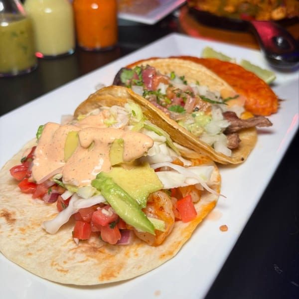 Three vibrant Mexican tacos, one shrimp, one beef, and one al pastor, on a white plate.