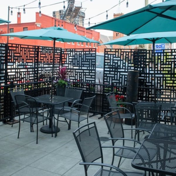 Mezcal Mexican Bar & Kitchen's outdoor patio with black tables, chairs, teal umbrellas, and string lights.