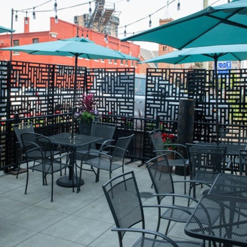 Mezcal Mexican Bar & Kitchen's outdoor patio with black tables, chairs, teal umbrellas, and string lights.