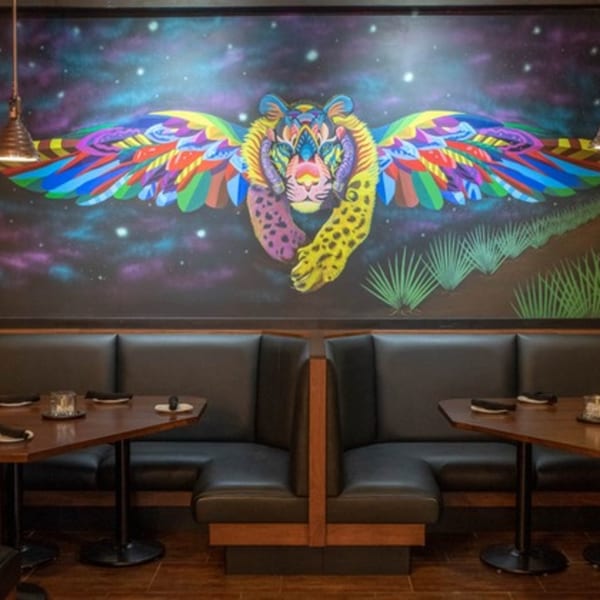 Mezcal Mexican Bar & Kitchen interior with a colorful winged jaguar mural above booth seating.